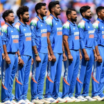A row of cricket players in blue uniforms, each with the word India on their jerseys, stand focused with their right hands on their hearts. Stadium seating and spectators blur in the background, setting the stage for an exciting India vs Bangladesh series. | jeetwinbet.com